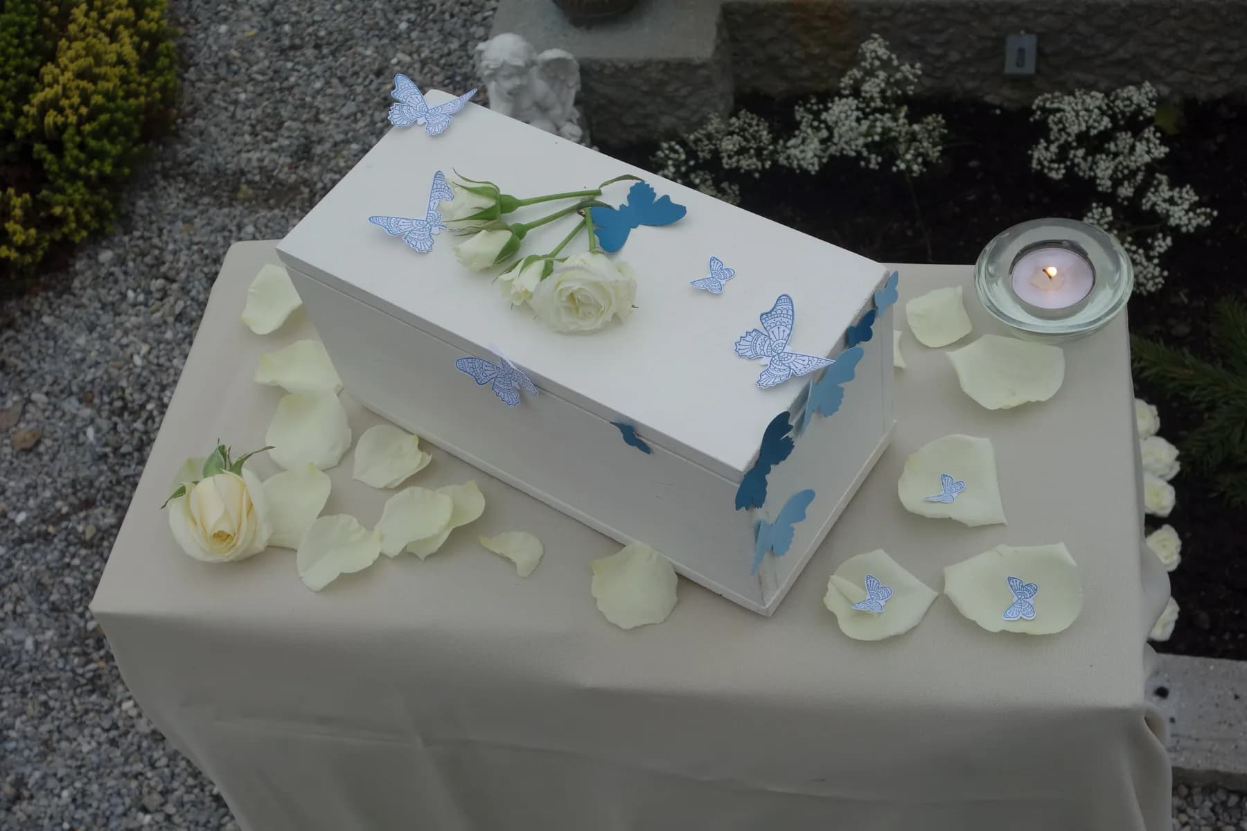 Kleiner weißer Sarg mit Schmetterlingen und Rosenblättern bei der Verabschiedung eines Sternenkindes